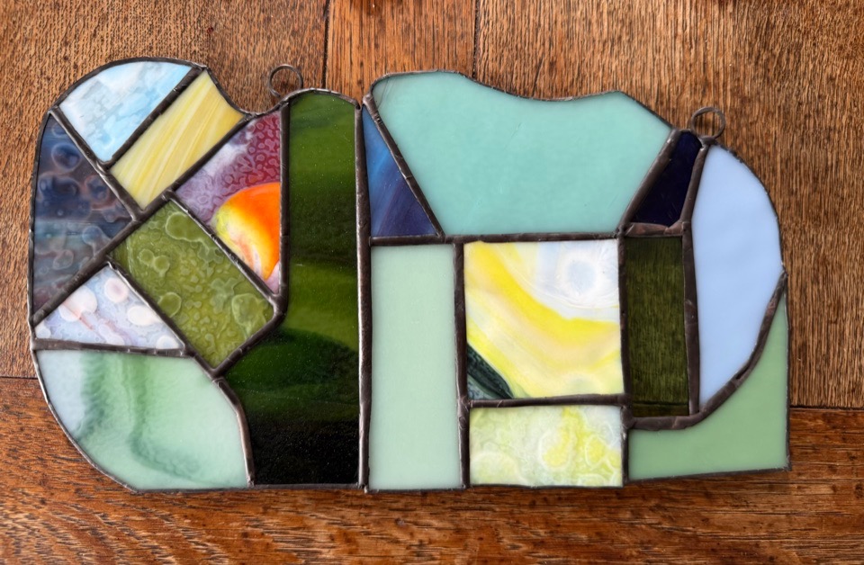 An abstract stained-glass panel in green, blue, yellow, and purple glass on a wooden surface